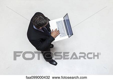 Businessman standing in lobby, using laptop computer View Large Photo Image Stock Image - Businessman standing in lobby, using laptop computer. Fotosearch