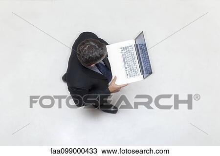 Stock Image - Businessman standing in lobby, using laptop computer. Fotosearch