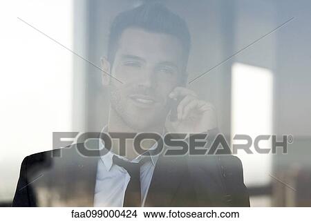 Businessman talking on cell phone, viewed through window View Large Photo Image Picture - Businessman talking on cell phone, viewed through window. Fotosearch