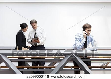 Businessman talking on cell phone, colleagues using digital tablet nearby View Large Photo Image Stock Photo - Businessman talking on cell phone, colleagues using digital tablet nearby. Fotosearch