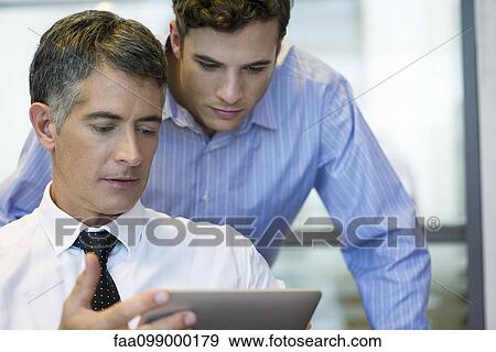 Stock Photo - Businessmen collaborating using digital tablet. Fotosearch