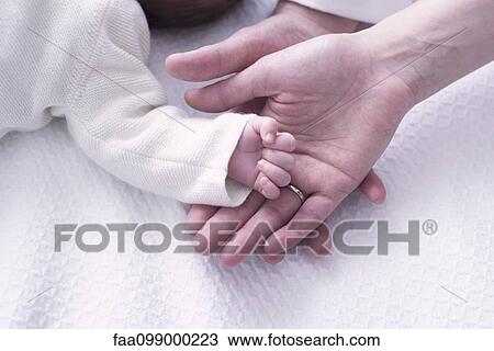 Stock Image - Close-up of baby's hand resting on parents' hands. Fotosearch