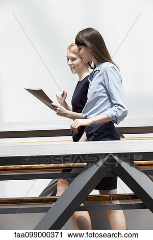 Colleagues walking in corridor and discussing file together View Large Photo Image Stock Image - Colleagues walking in corridor and discussing file together. Fotosearch