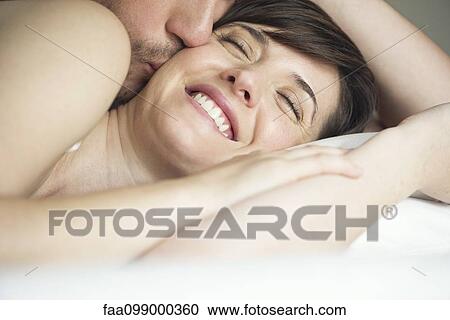 Stock Image - Couple cuddling in bed, husband kissing wife. Fotosearch