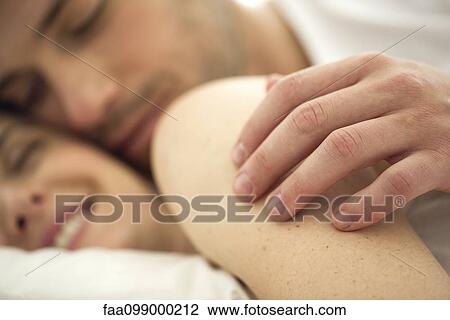 Couple cuddling together in bed, husband's hand on wife's shoulder, close-up View Large Photo Image Stock Image - Couple cuddling together in bed, husband's hand on wife's shoulder, close-up. Fotosearch