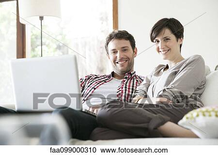 Couple relaxing together on sofa with laptop computer View Large Photo Image Stock Image - Couple relaxing together on sofa with laptop computer. Fotosearch