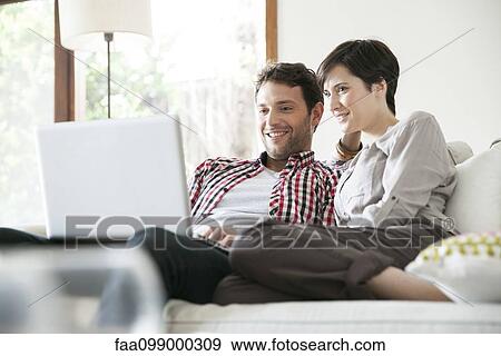 Stock Photo - Couple relaxing together on sofa with laptop computer. Fotosearch