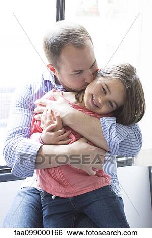 Father holding daughter on his lap, kissing her cheek View Large Photo Image Stock Photograph - Father holding daughter on his lap, kissing her cheek. Fotosearch