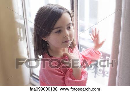 Stock Photo - Girl standing by window, looking away in thought. Fotosearch