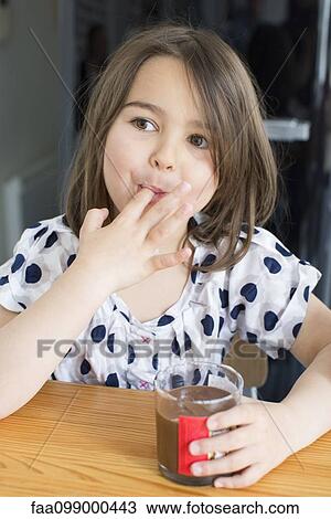 Stock Image - Little girl eating chocolate sauce from a jar with her fingers. Fotosearch