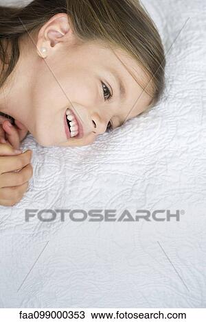 Stock Image - Little girl lying on bed, high angle view. Fotosearch