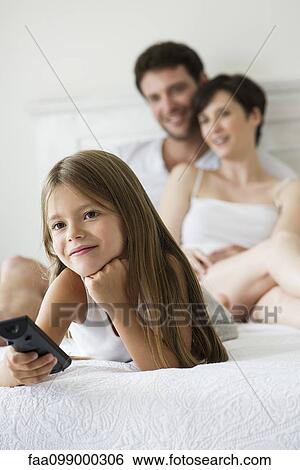Stock Photograph - Little girl watching tv in bedroom with parents. Fotosearch