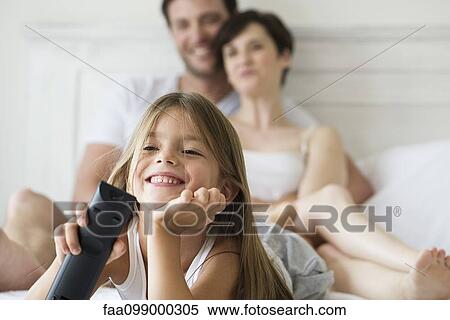 Stock Photography - Little girl watching tv in bedroom with parents. Fotosearch