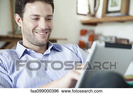 Stock Photograph - Man using digital tablet at home. Fotosearch