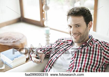 Stock Photography - Man using smartphone at home, smiling. Fotosearch