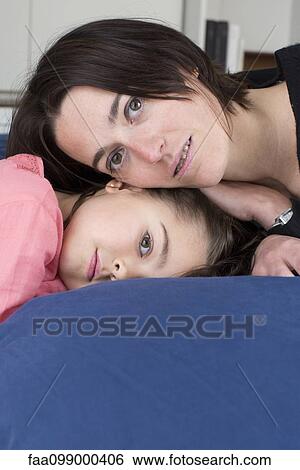 Stock Photograph - Mother and daughter lying together on bed, portrait. Fotosearch