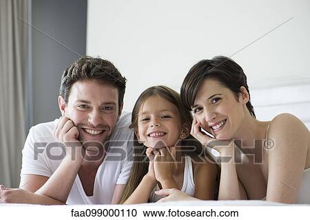 Stock Image - Parents and daughter lying on bed together, portrait. Fotosearch