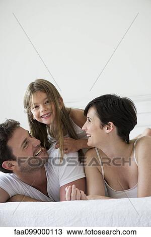 Stock Image - Parents and daughter lying on bed together, portrait. Fotosearch