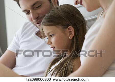 Stock Image - Parents and daughter reading together. Fotosearch