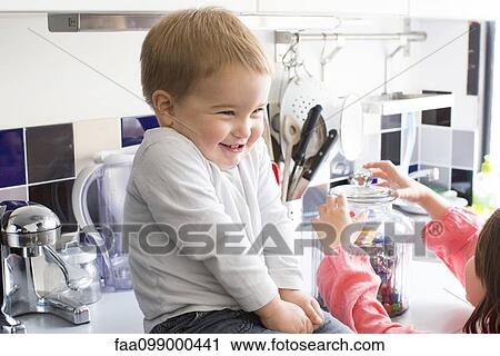 Toddler boy sitting on kitchen counter, smiling as sister reaches for candy jar View Large Photo Image Stock Image - Toddler boy sitting on kitchen counter, smiling as sister reaches for candy jar. Fotosearch