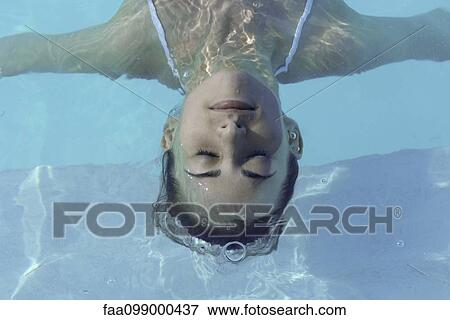 Stock Photo - Woman floating in pool, eyes closed, high angle view. Fotosearch