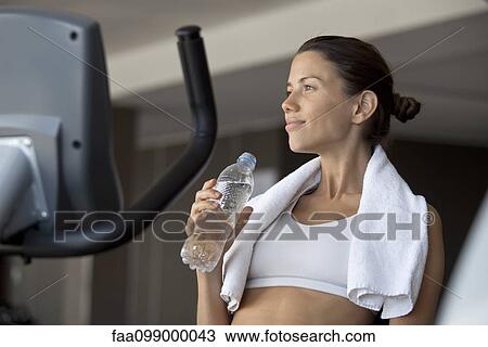Woman holding bottle of water in health club View Large Photo Image Stock Image - Woman holding bottle of water in health club. Fotosearch