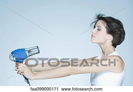 Stock Image - Woman holding out hair dryer, profile. Fotosearch