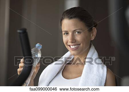 Stock Photograph - Woman hydrating with bottled water in health club. Fotosearch