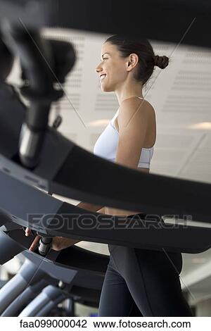 Stock Image - Woman on exercise machine at gym. Fotosearch