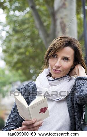 Woman reading paperback book outdoors View Large Photo Image Stock Image - Woman reading paperback book outdoors. Fotosearch