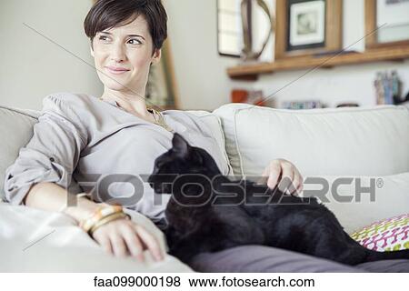 Stock Photo - Woman relaxing on sofa with cat on her lap. Fotosearch