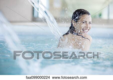 Picture - Woman relaxing under fountain in swimming pool. Fotosearch