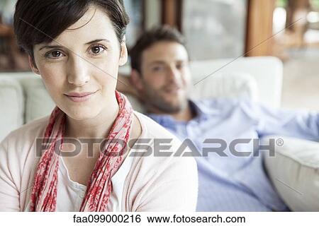 Woman sitting in living room with husband in background, portrait View Large Photo Image Stock Photograph - Woman sitting in living room with husband in background, portrait. Fotosearch