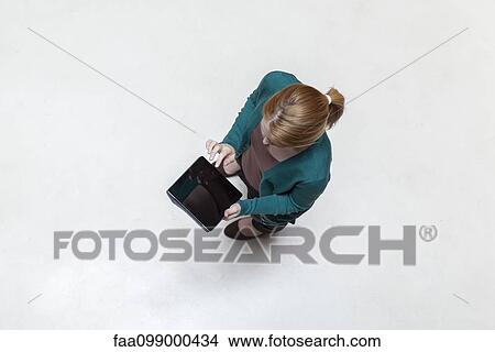 Woman standing in lobby, using digital tablet, overhead view View Large Photo Image Picture - Woman standing in lobby, using digital tablet, overhead view. Fotosearch