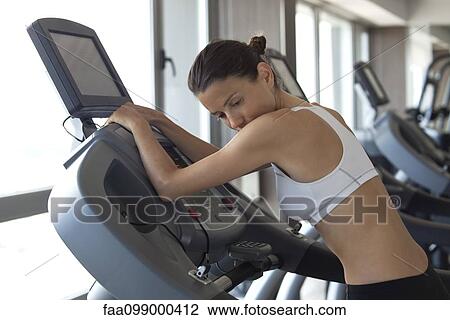 Stock Image - Woman using exercise machine in health club. Fotosearch