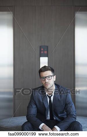 Stock Photo - Young businessman sitting in lobby, portrait. Fotosearch