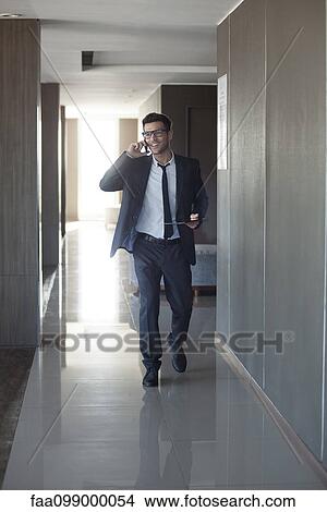 Picture - Young businessman talking on phone while walking through office. Fotosearch