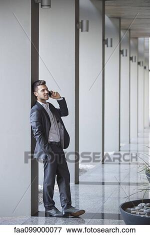 Young executive taking phone call while leaning against column in building lobby View Large Photo Image Stock Photo - Young executive taking phone call while leaning against column in building lobby. Fotosearch