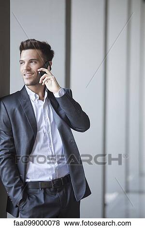 Stock Photo - Young man leaning against buiding column talking on cell phone. Fotosearch