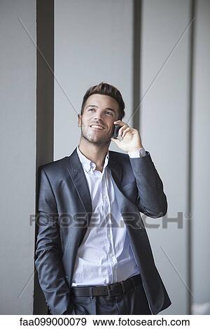 Stock Photo - Young man leaning against buiding column talking on cell phone. Fotosearch