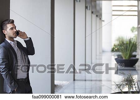 Stock Image - Young man talking on cell phonel in building lobby. Fotosearch