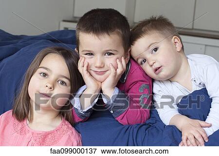 Stock Photo - Young siblings relaxing together on bed, portrait. Fotosearch