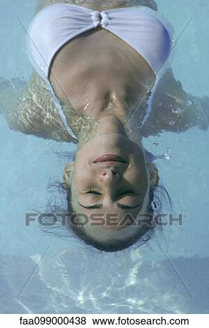 Stock Photo - Young woman floating in swimming pool, eyes closed. Fotosearch
