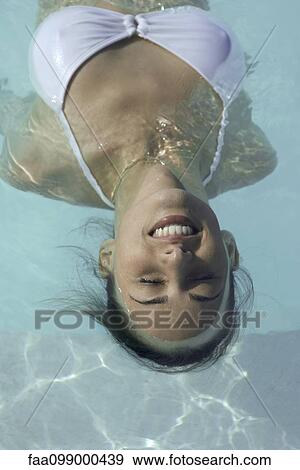 Stock Photo - Young woman floating in swimming pool, smiling. Fotosearch