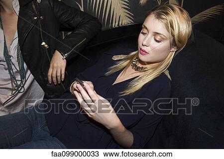 Young woman reclining on sofa using smartphone View Large Photo Image Stock Image - Young woman reclining on sofa using smartphone. Fotosearch
