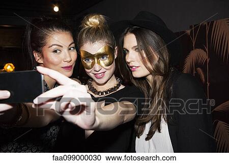 Stock Image - Young women at night club taking selfie. Fotosearch