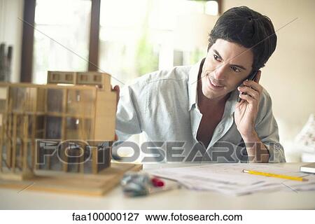 Stock Photo - Architect talking on cell phone at desk. Fotosearch
