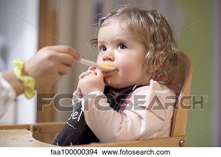 Picture - Baby girl being fed by parent, cropped. Fotosearch