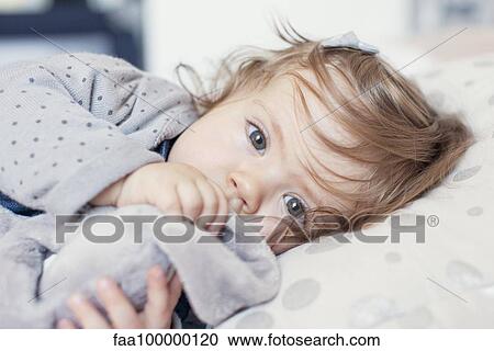 Stock Image - Baby girl lying down, sucking thumb, portrait. Fotosearch