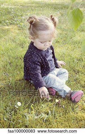 Stock Image - Baby girl sitting on grass, picking flower. Fotosearch